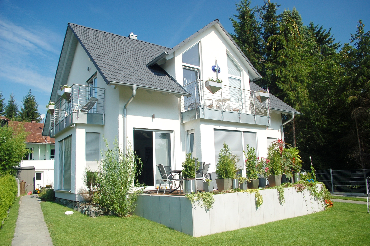 Montage Mündlein – Bauen und Renovieren – Wohnzimmer mit weißen Wänden und Holzboden; eine offene Terrassentür führt auf den Balkon.