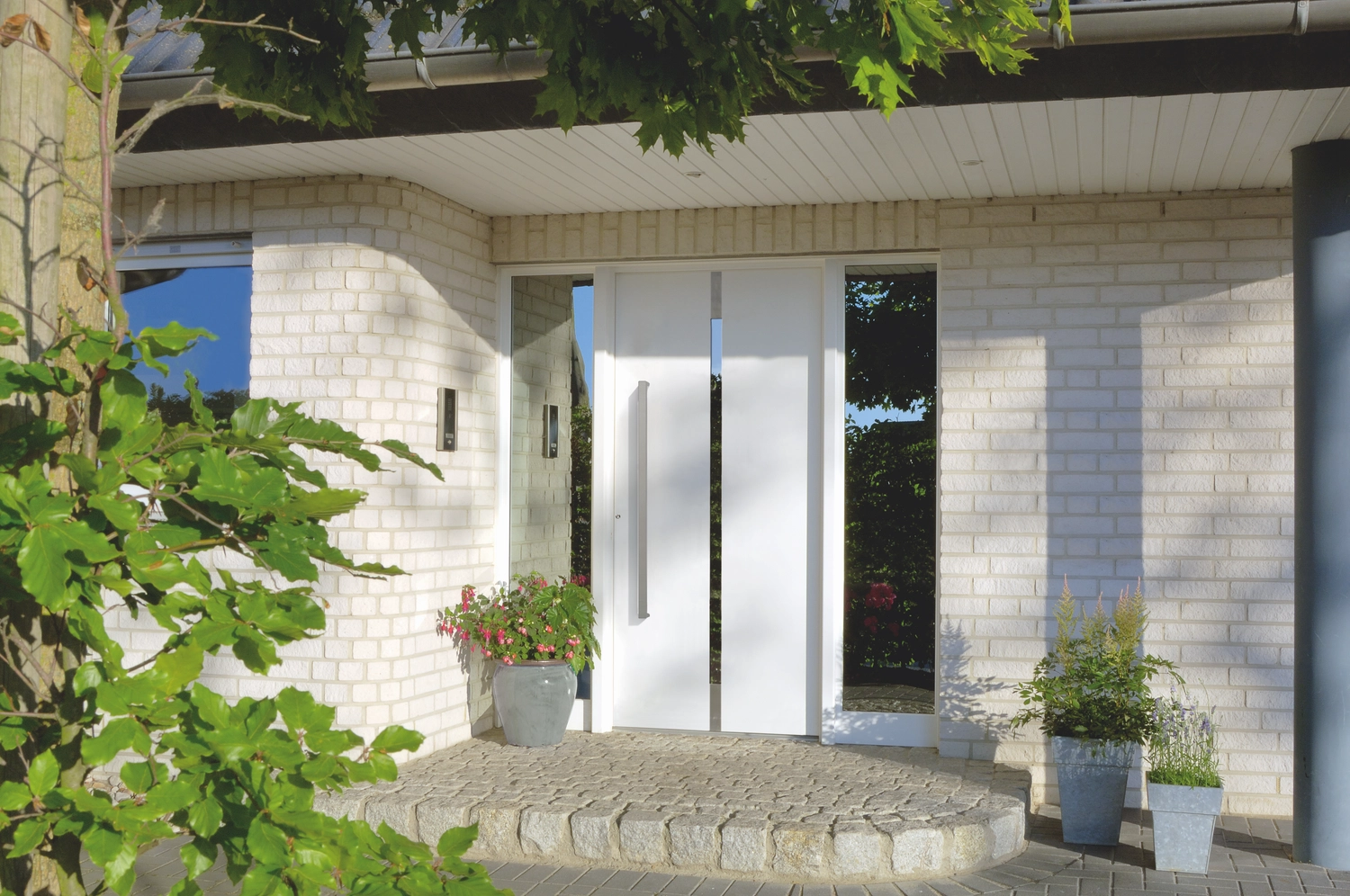 Montage Mündlein – Bauen und Renovieren – Eine graue, moderne Landhaus-Eingangstür mit überdachter Veranda, Holzeingangstür mit Glasfenster und grauer Vinyl- und Holzverkleidung.
